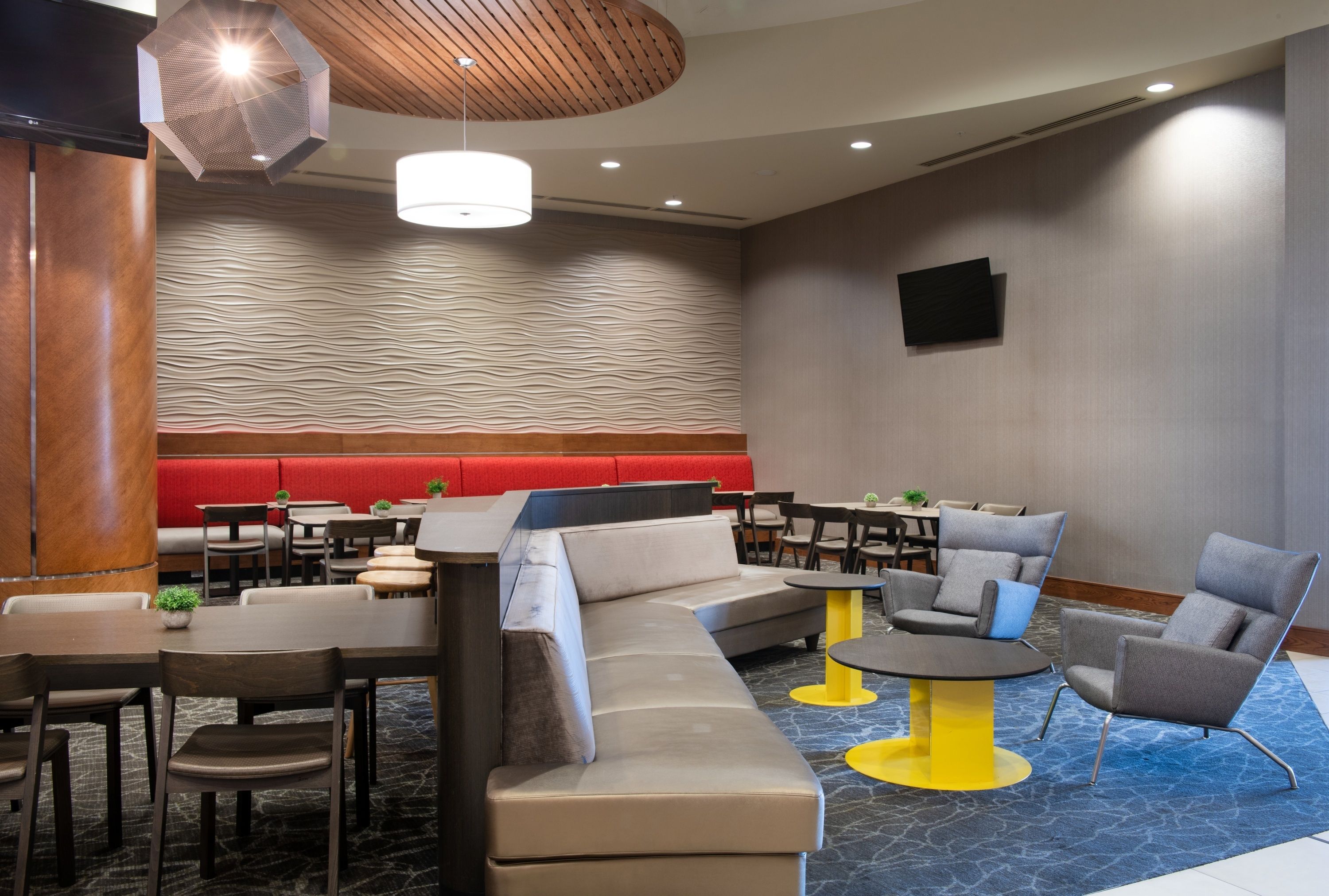 En modern hotellobby med en modulsoffa, runda bord och en avskild sittgrupp med röda sittplatser.