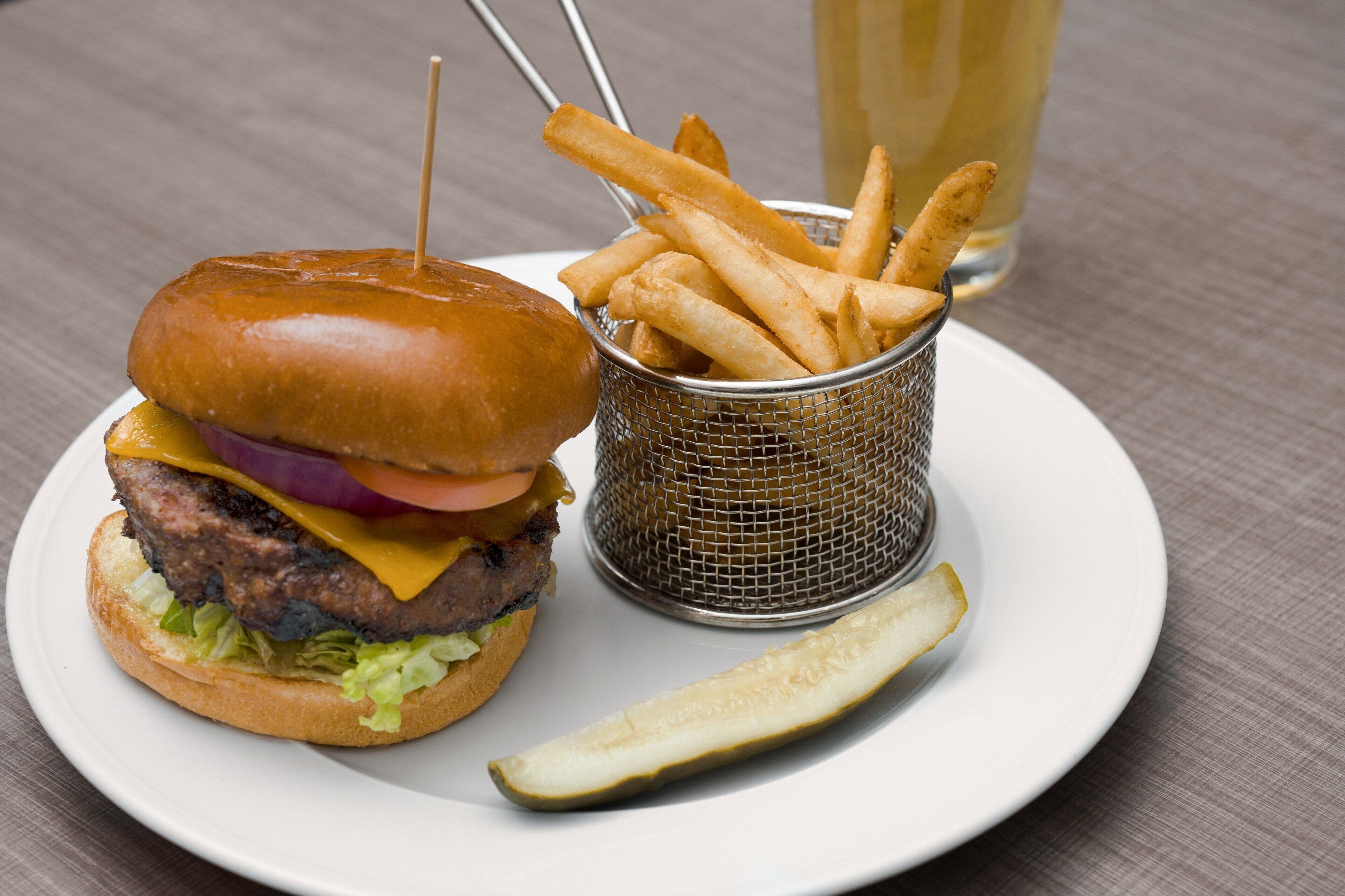 Un plato con una hamburguesa, papas fritas y un pepinillo.