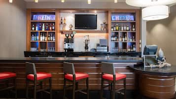 A bar area with a TV, shelves of liquor bottles, and a bar counter with stools.