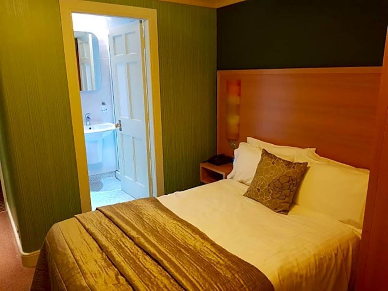 A hotel room with a bed, a nightstand, a mirror, and a door leading to a bathroom.