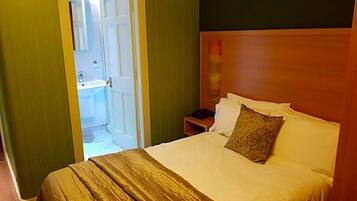 A hotel room with a bed, a nightstand, a mirror, and a door leading to a bathroom.