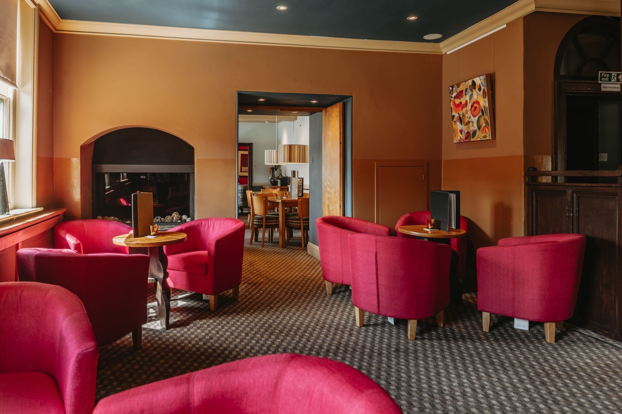 Un vestíbulo de hotel con sillones tapizados en rojo, una chimenea, un comedor y un cuadro en la pared.