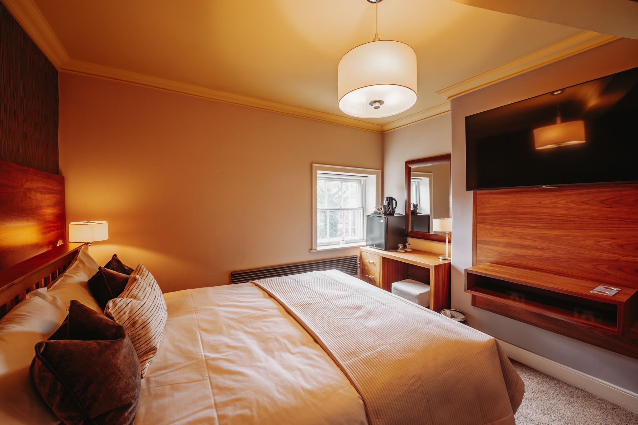 A hotel room with a bed, bedside table, lamp, TV, and a large mirror.