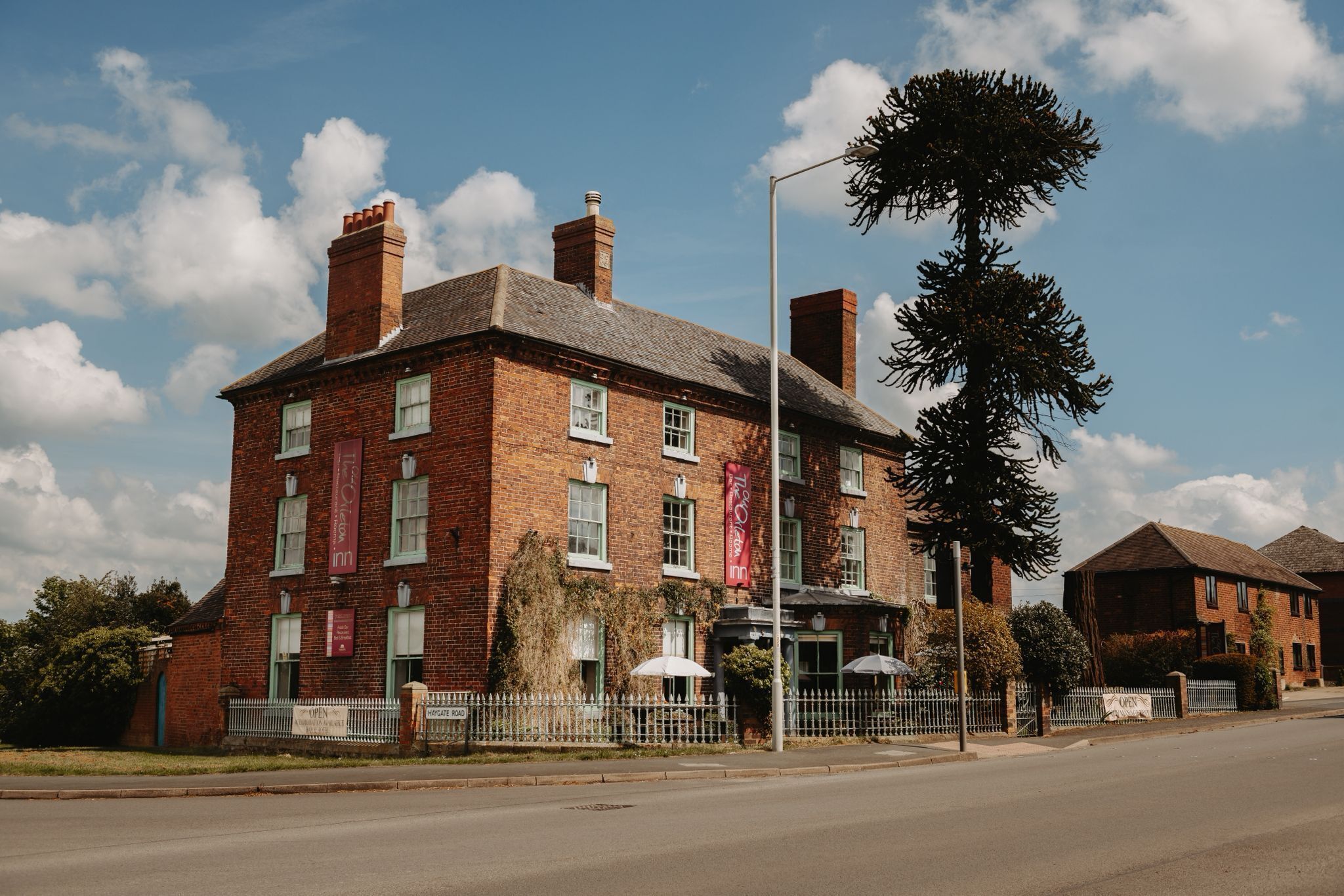 A brick building with a prominent chimney, a flag, and a tree in front.