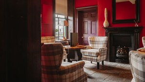 A room with a fireplace, plaid chairs, a table, and a red wall. - The Old Orleton Inn (Telford)