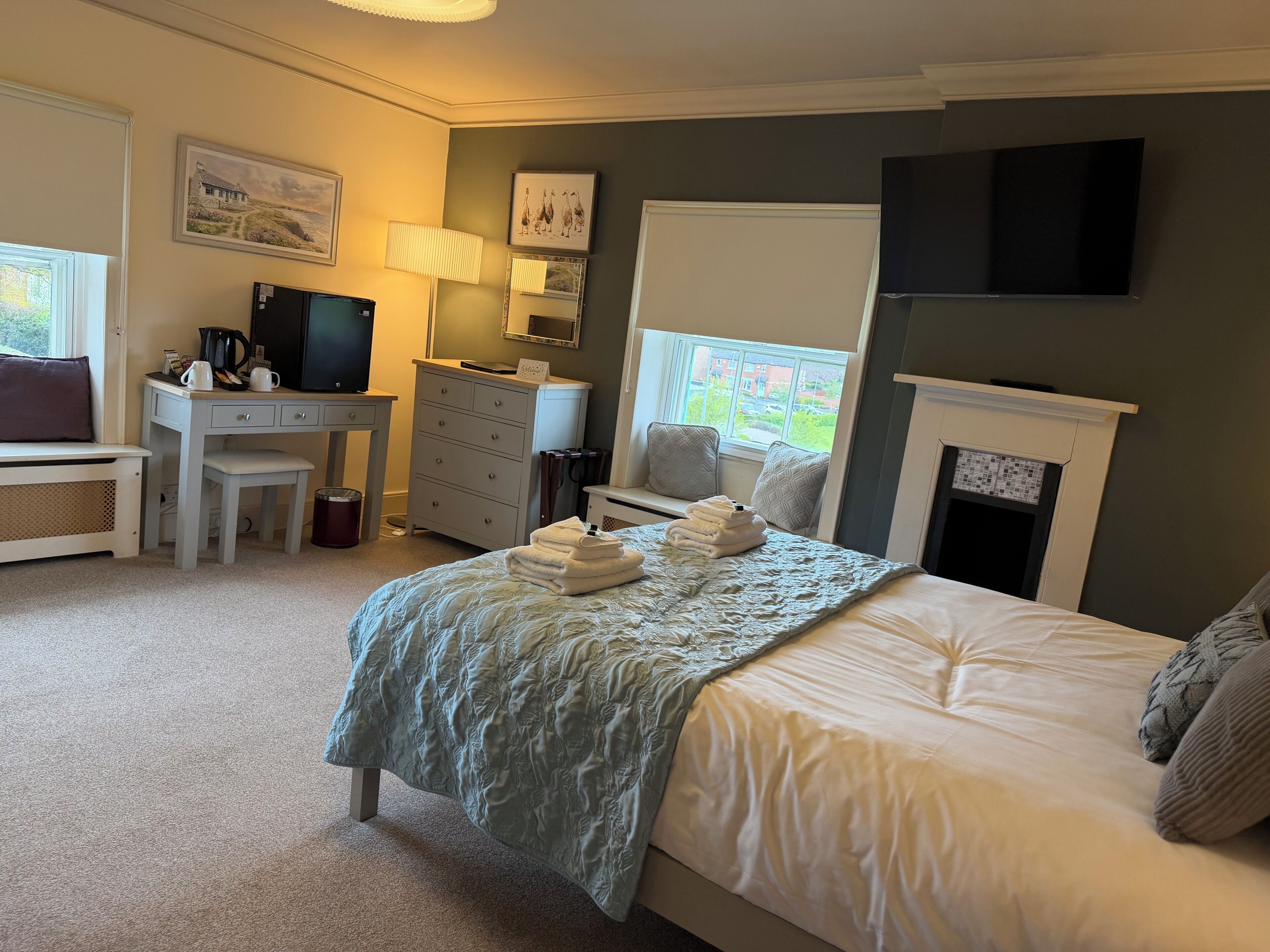 A bedroom with a bed, a desk, a television, a fireplace, and a window.