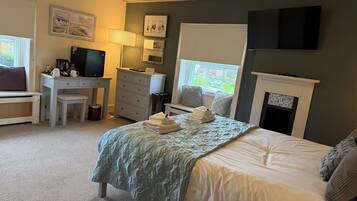 A bedroom with a bed, a desk, a television, a fireplace, and a window.