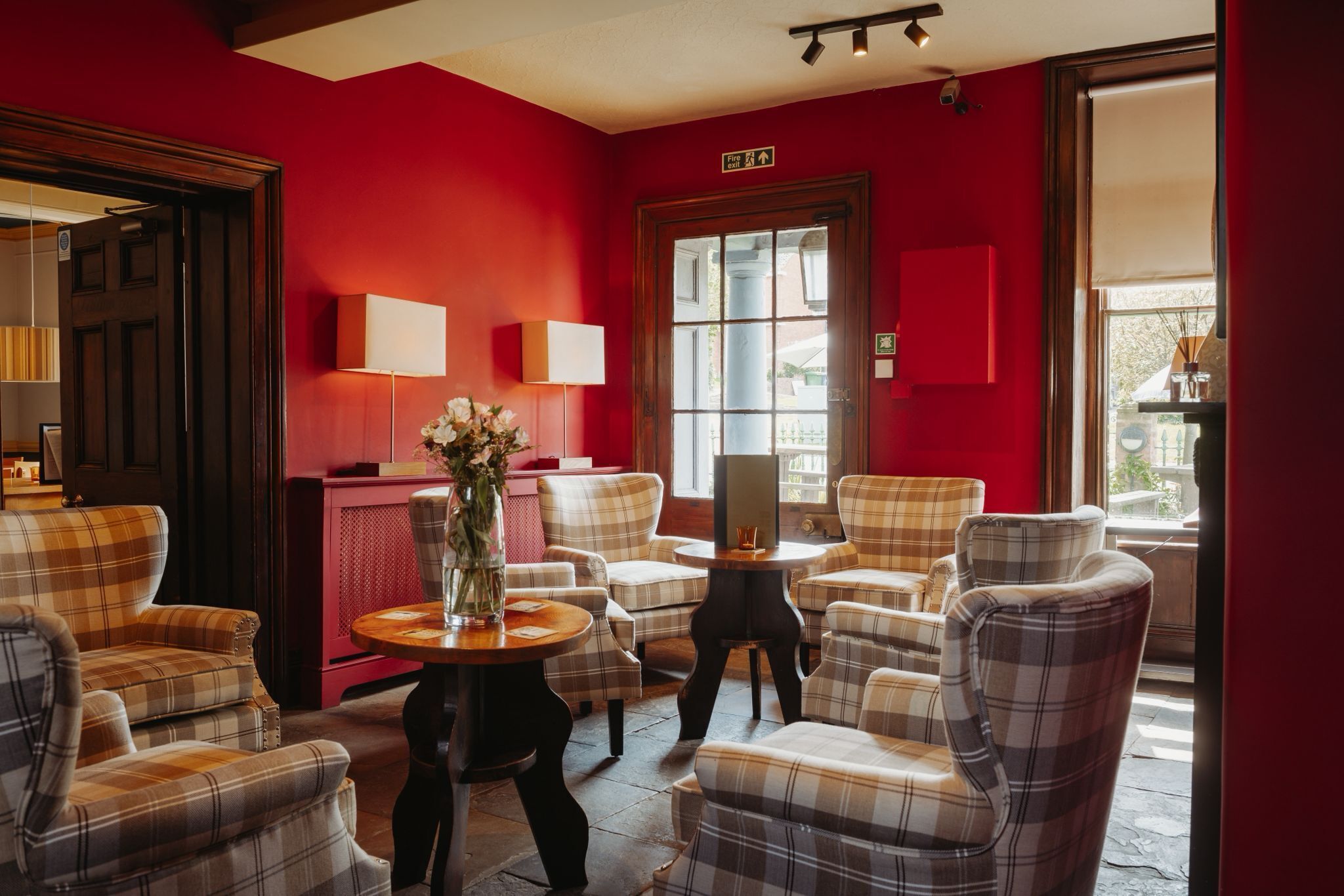 A room with plaid chairs, a vase with flowers, a small table, and a red wall.