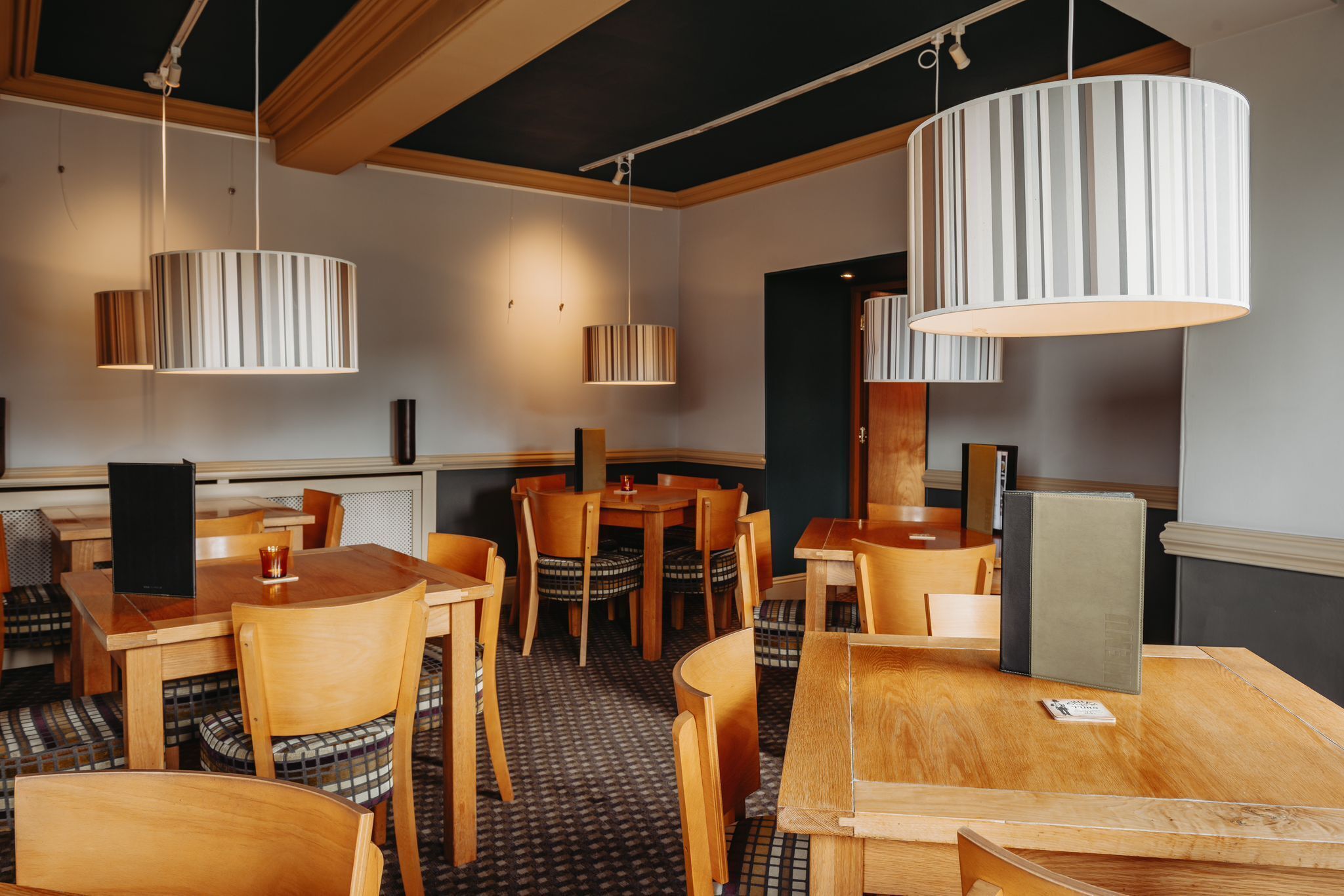 A restaurant with wooden tables and chairs, striped pendant lights, and a checkered floor pattern.