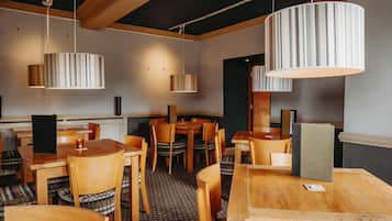 A restaurant with wooden tables and chairs, striped pendant lights, and a checkered floor pattern.