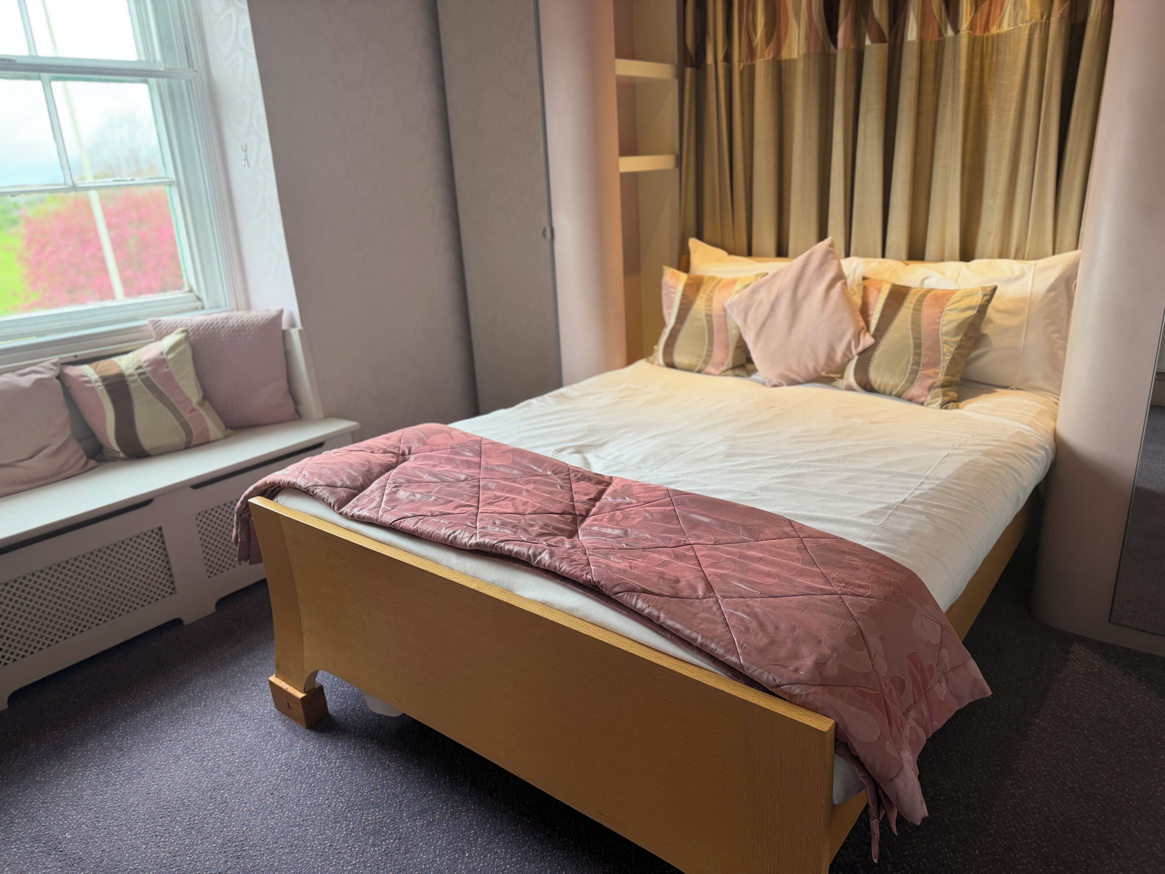 A bedroom with a wooden bed, a window with curtains, and a radiator.