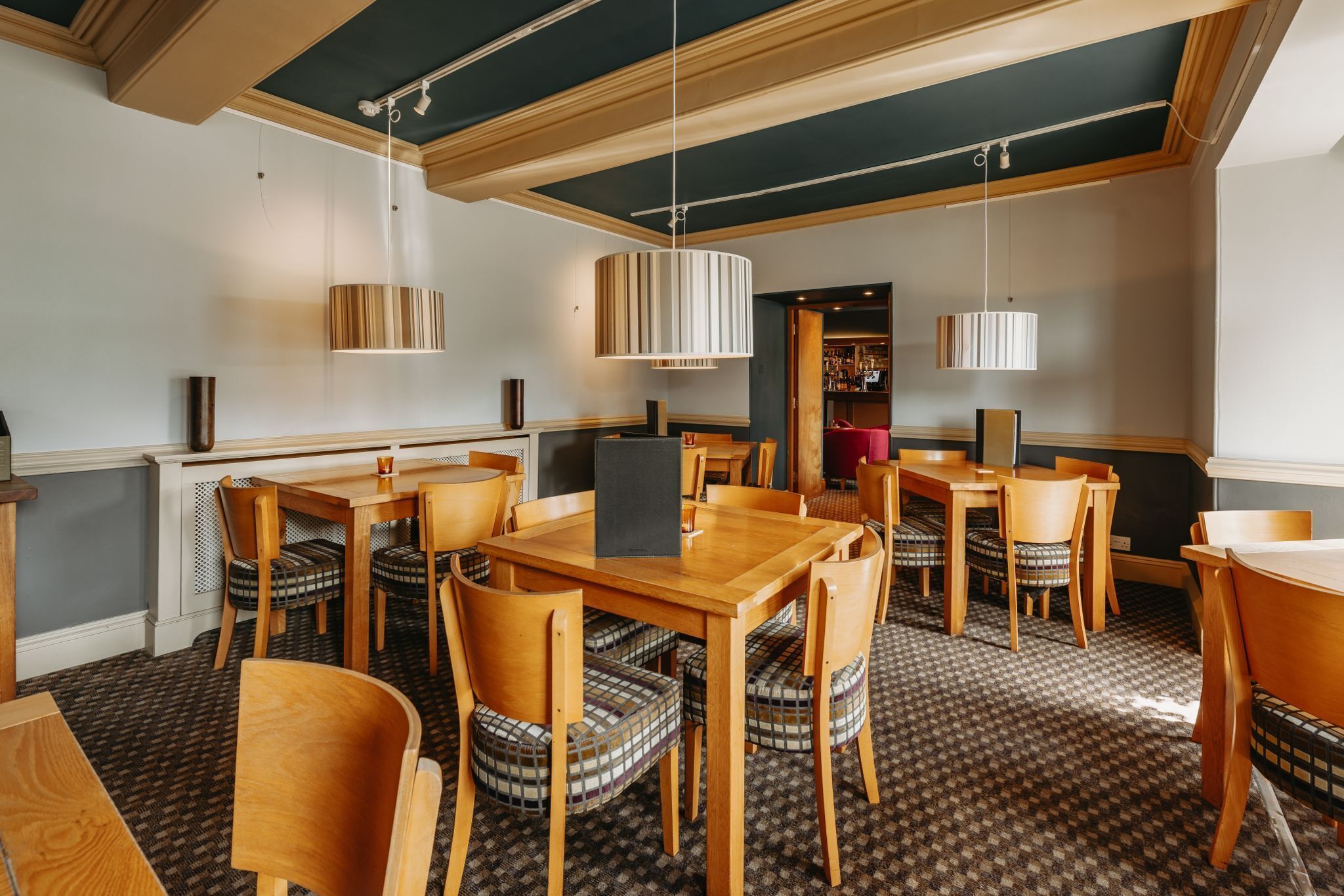 A restaurant with wooden tables and chairs, striped lamps, and a patterned carpet.