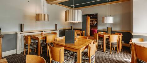 A restaurant with wooden tables and chairs, striped lamps, and a patterned carpet.