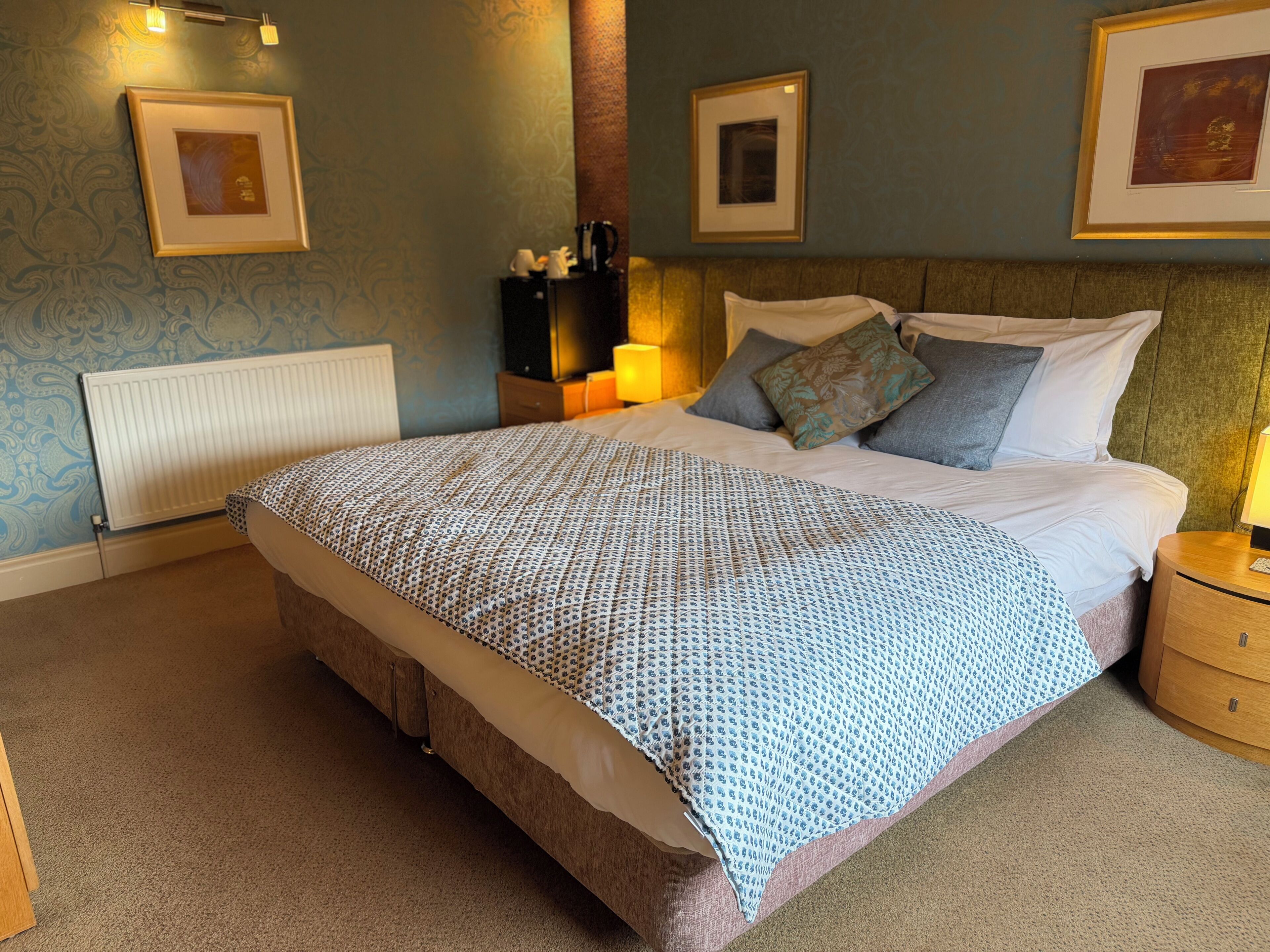 A bedroom with a bed, bedside tables, a radiator, and framed pictures on the walls.