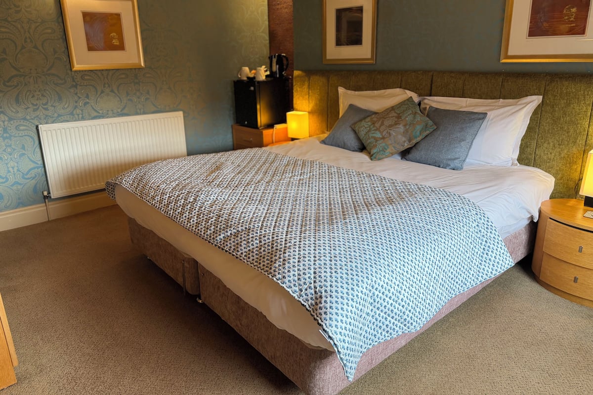 A bedroom with a bed, bedside tables, a radiator, and framed pictures on the walls.