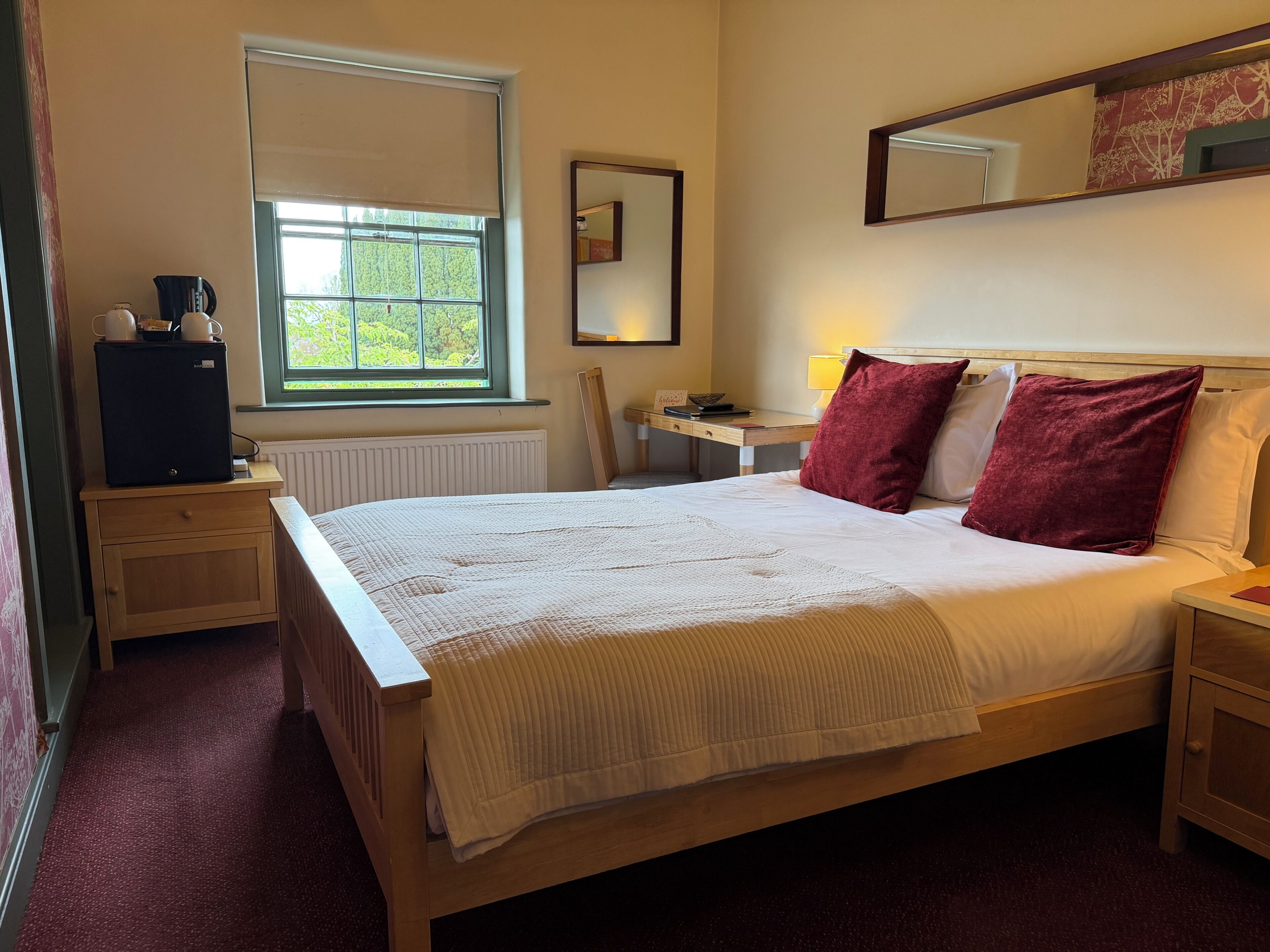 A bedroom with a bed, a desk, a chair, a radiator, a window, and a mirror.