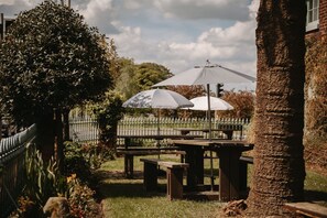 A garden area with picnic tables and umbrellas, surrounded by a fence and trees.