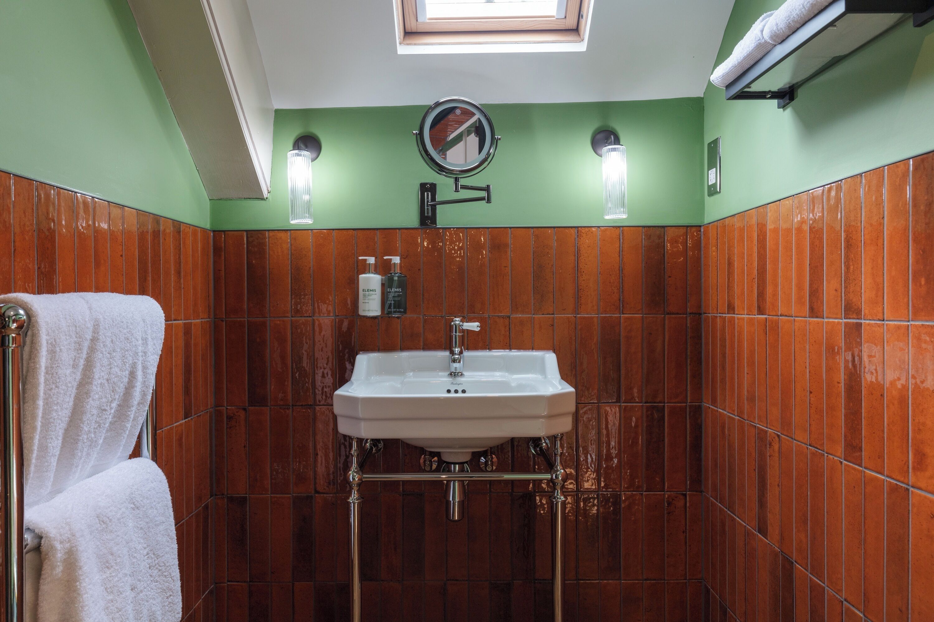 A bathroom with a white sink, green walls, and a window above the mirror.