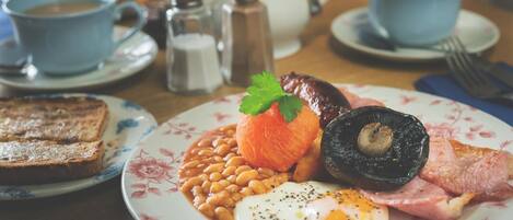 A breakfast plate with eggs, beans, bacon, and a tomato.