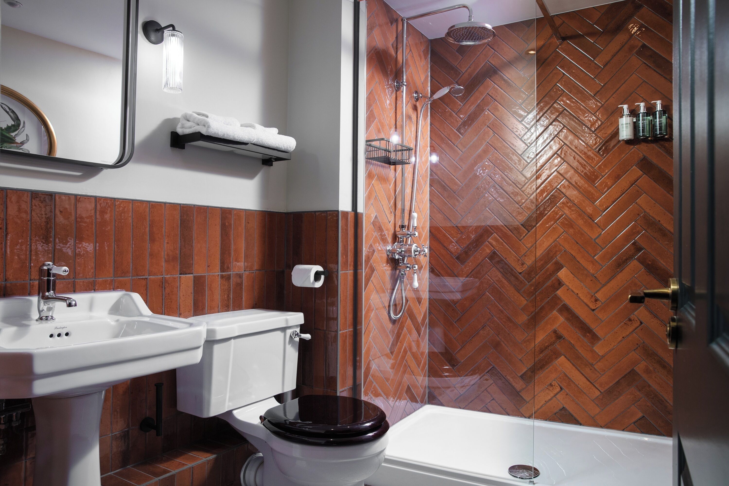 A bathroom with a herringbone-patterned tile wall, a white sink, a toilet, a glass-enclosed shower, and a white bathtub.