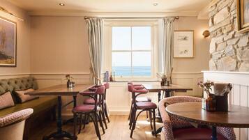 A dining area with a wooden table, cushioned seating, and a view of the sea through a window.