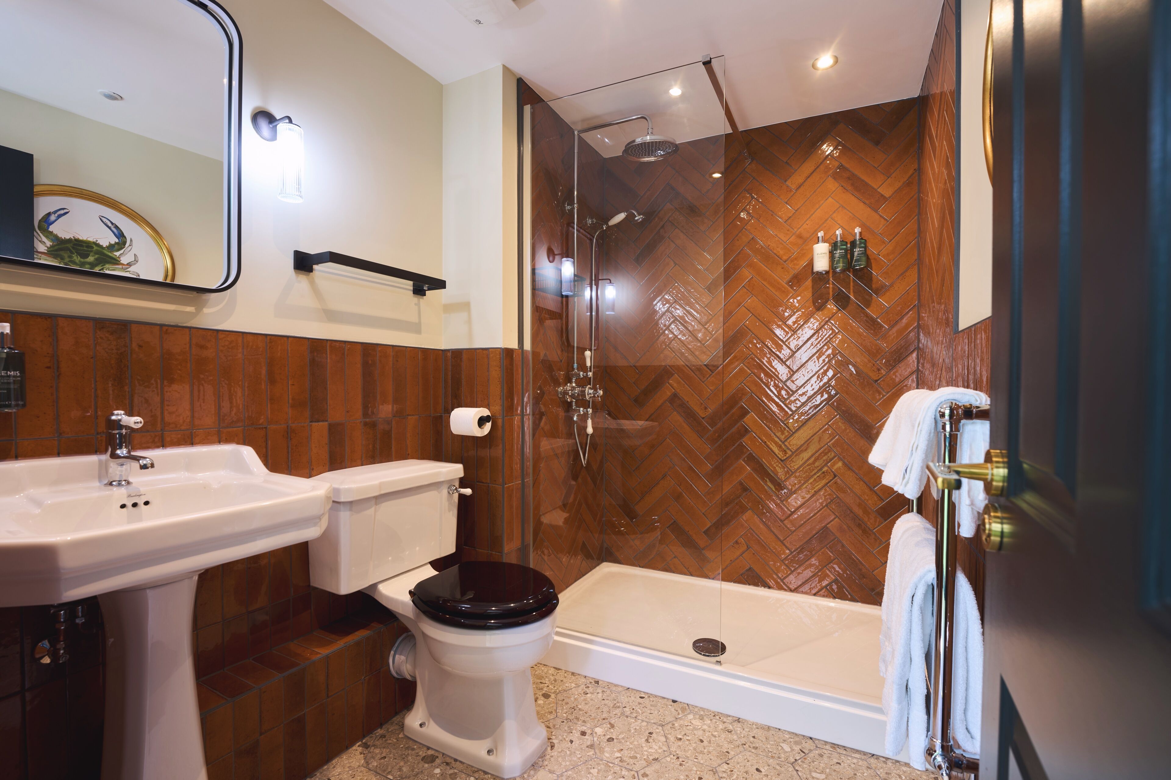 A modern bathroom with a wooden herringbone wall, a glass-enclosed shower, a white sink, and a toilet.