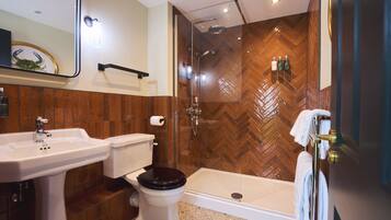 A modern bathroom with a wooden herringbone wall, a glass-enclosed shower, a white sink, and a toilet.