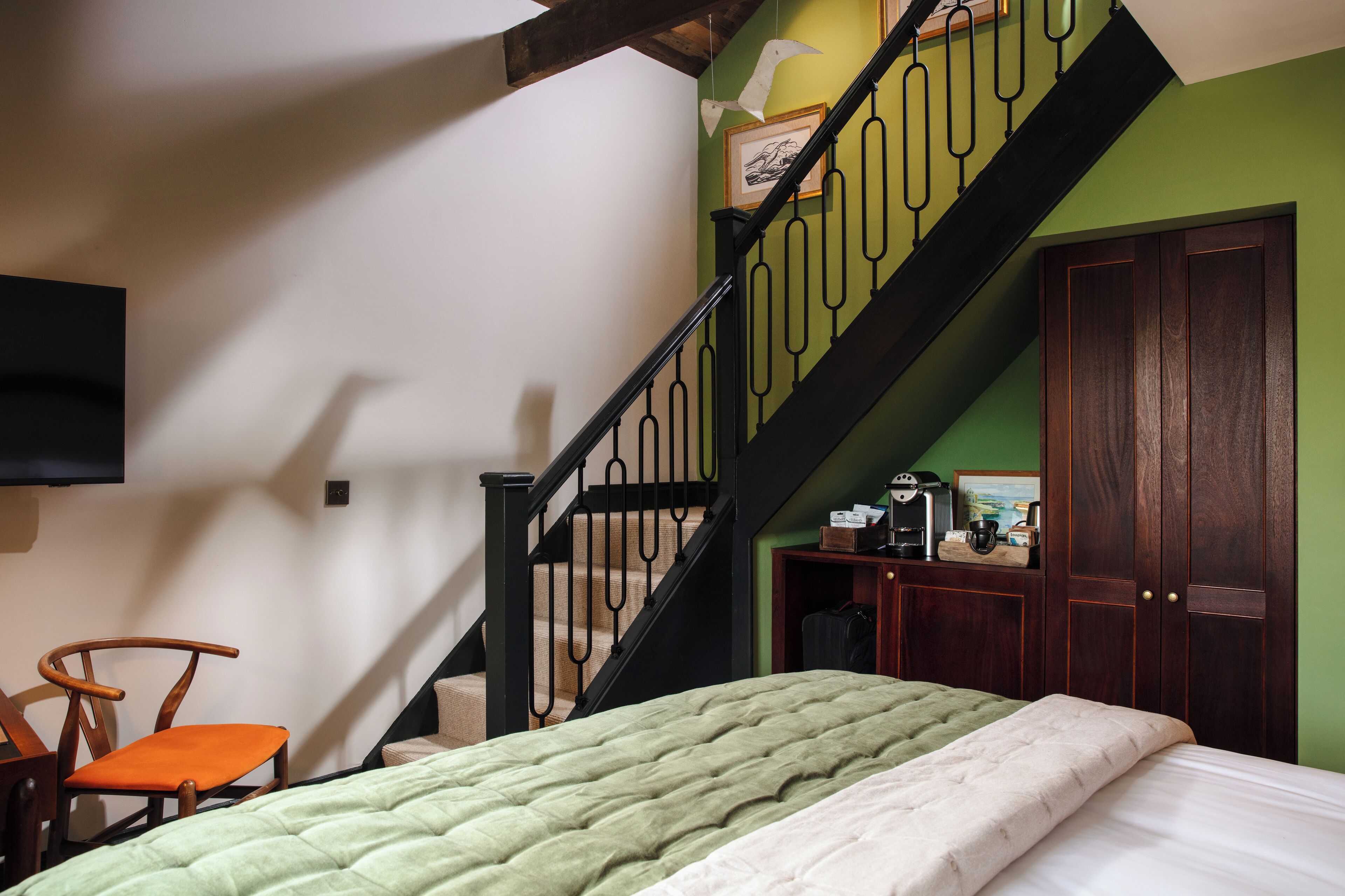 A bedroom with a bed, a chair, a staircase, and a wardrobe.