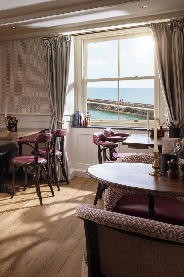 Un área de comedor con vista al mar, que cuenta con muebles de madera y una ventana con cortinas.