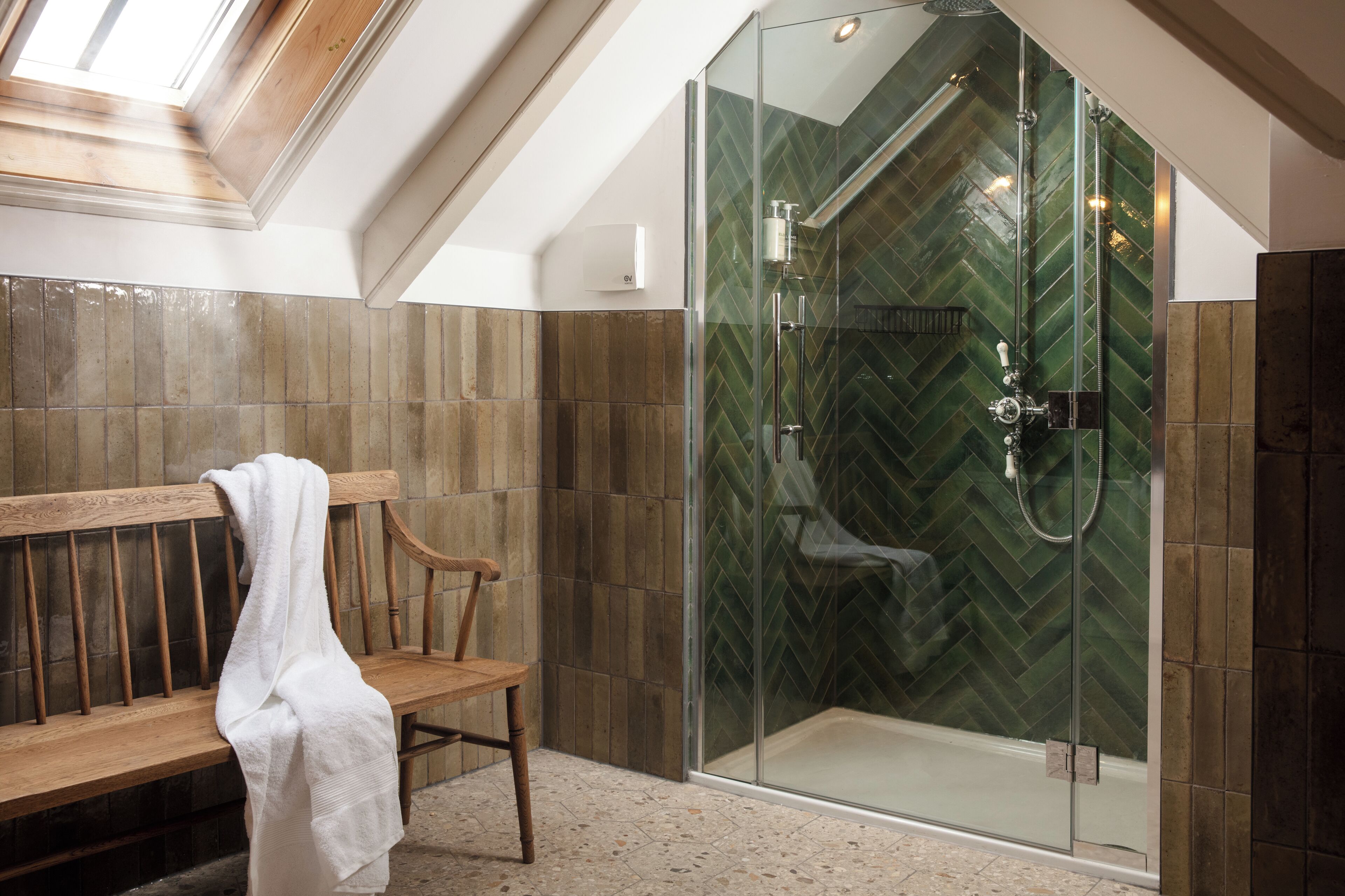 A shower with a glass door and a herringbone tile pattern on the walls.