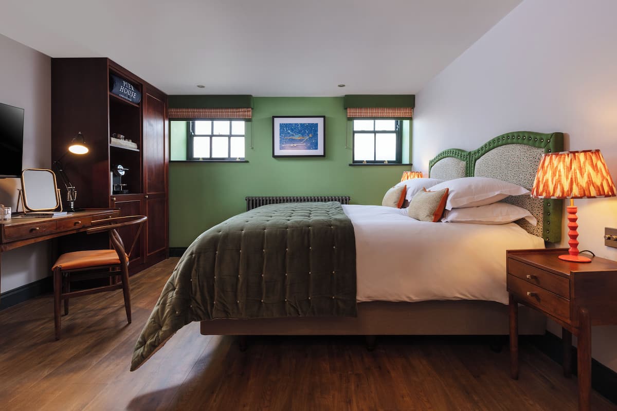 Un dormitorio ordenado con cama, mesita de noche, lámpara y un escritorio con silla.
