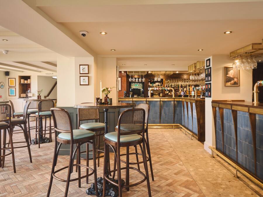Zona de bar con taburetes de madera, una barra con grifo de cerveza y estanterías llenas de botellas.