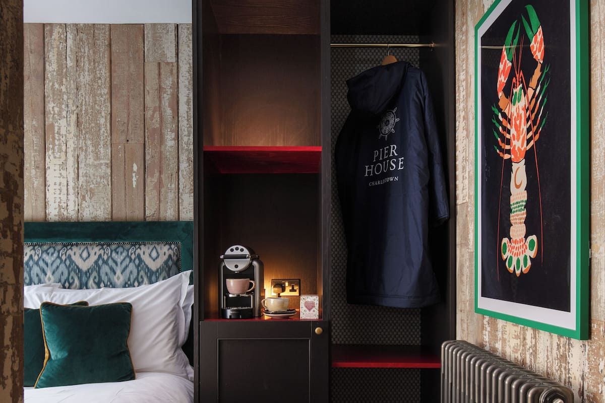 Una habitación de hotel pequeña con una cama, una cafetera, una bata colgada y una obra de arte enmarcada en la pared.