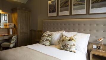 Un dormitorio ordenado con una cama grande, dos almohadas con estampado de paisaje, una mesita de noche con una lámpara, un armario de madera y cuadros en la pared.