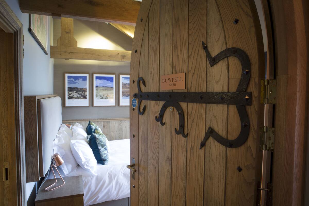 A wooden door with a sign reading "BOWFELL 295ft." and a bed with white bedding and pillows.