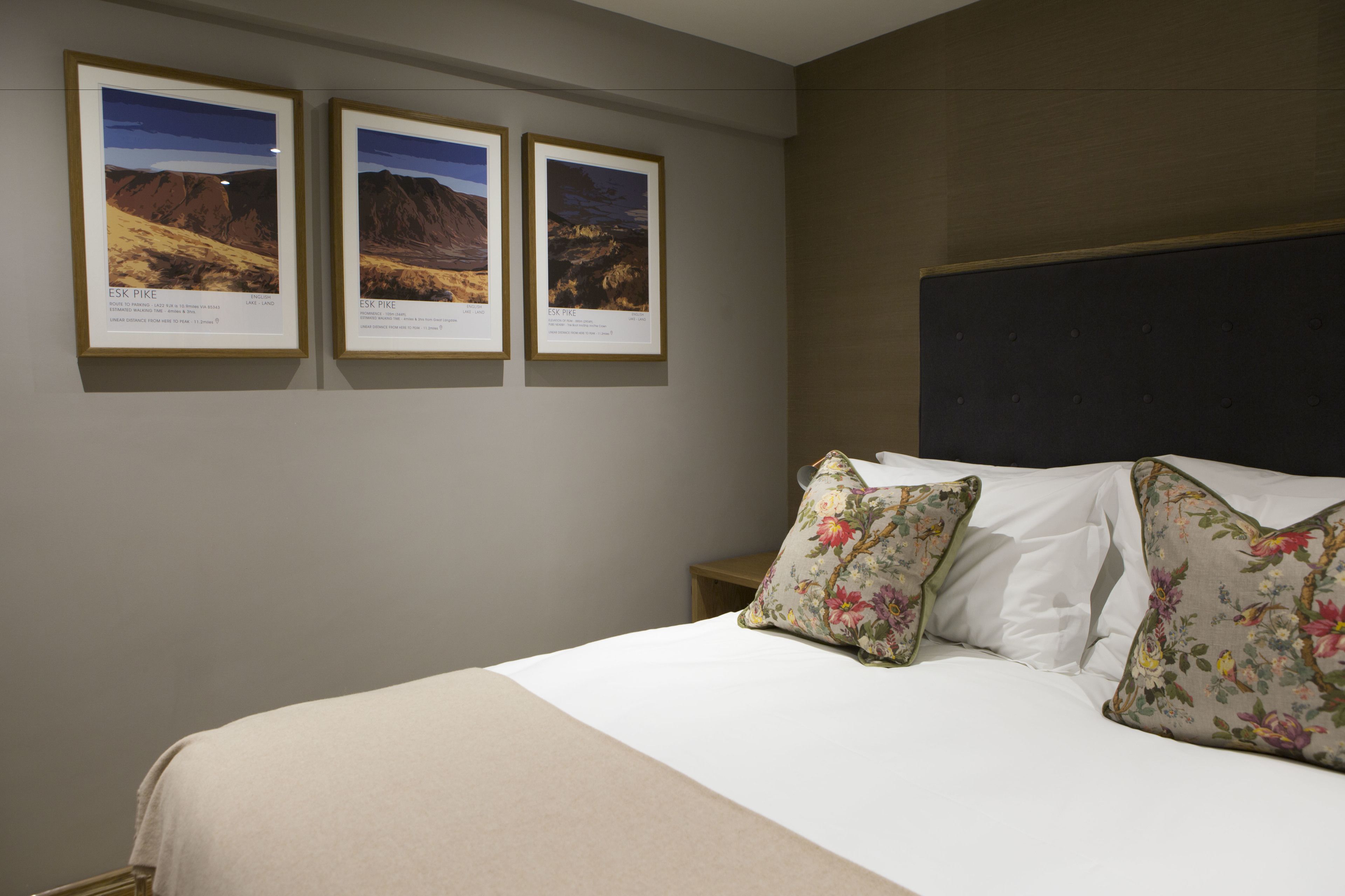 A hotel room with a bed, floral pillows, and three framed pictures on the wall.