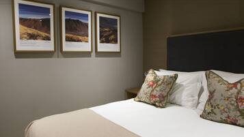 A hotel room with a bed, floral pillows, and three framed pictures on the wall.
