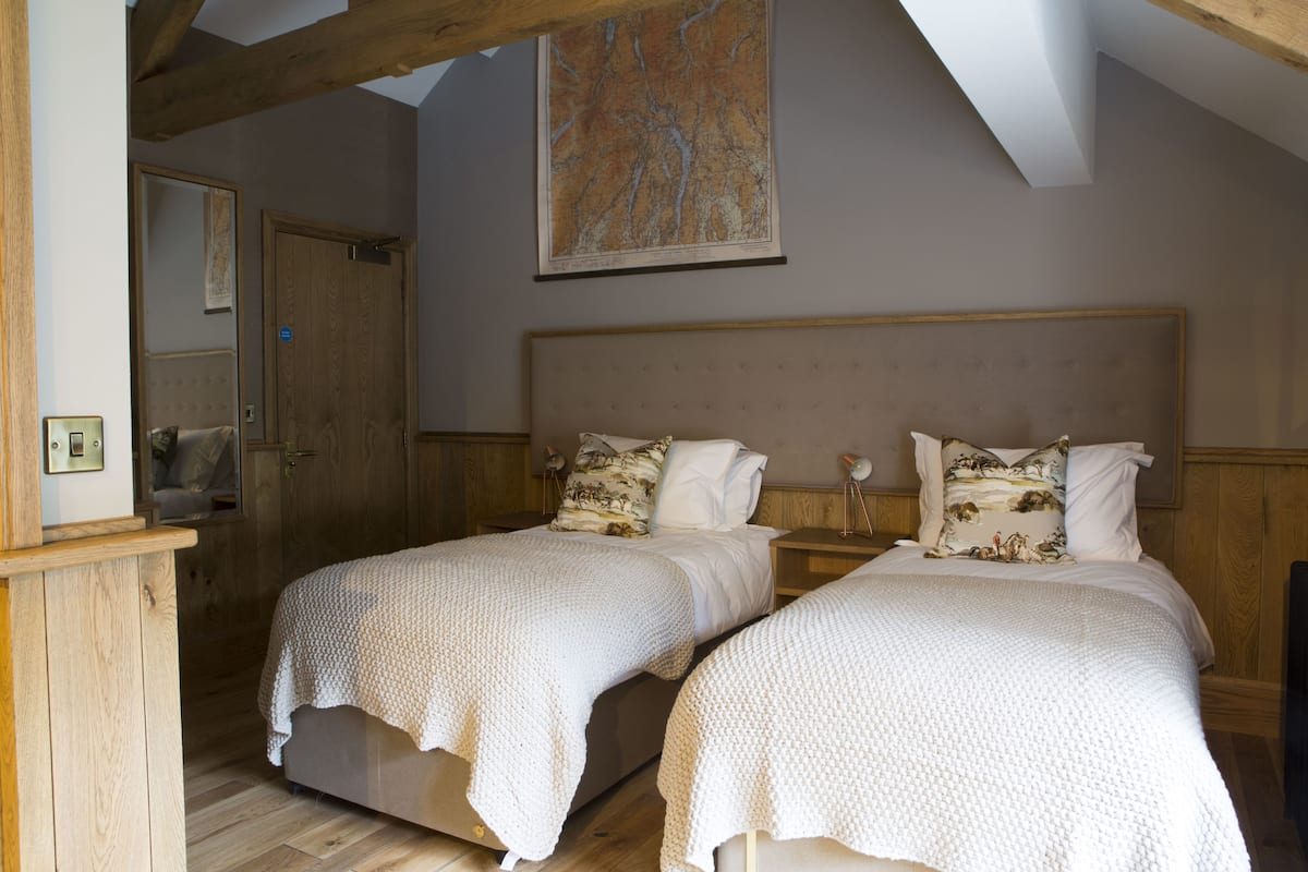 A bedroom with two single beds, wooden headboards, a large painting on the wall, and a wooden wardrobe.