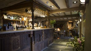 Zona de bar con mostrador de madera, suelo de piedra y pared de piedra al fondo.
