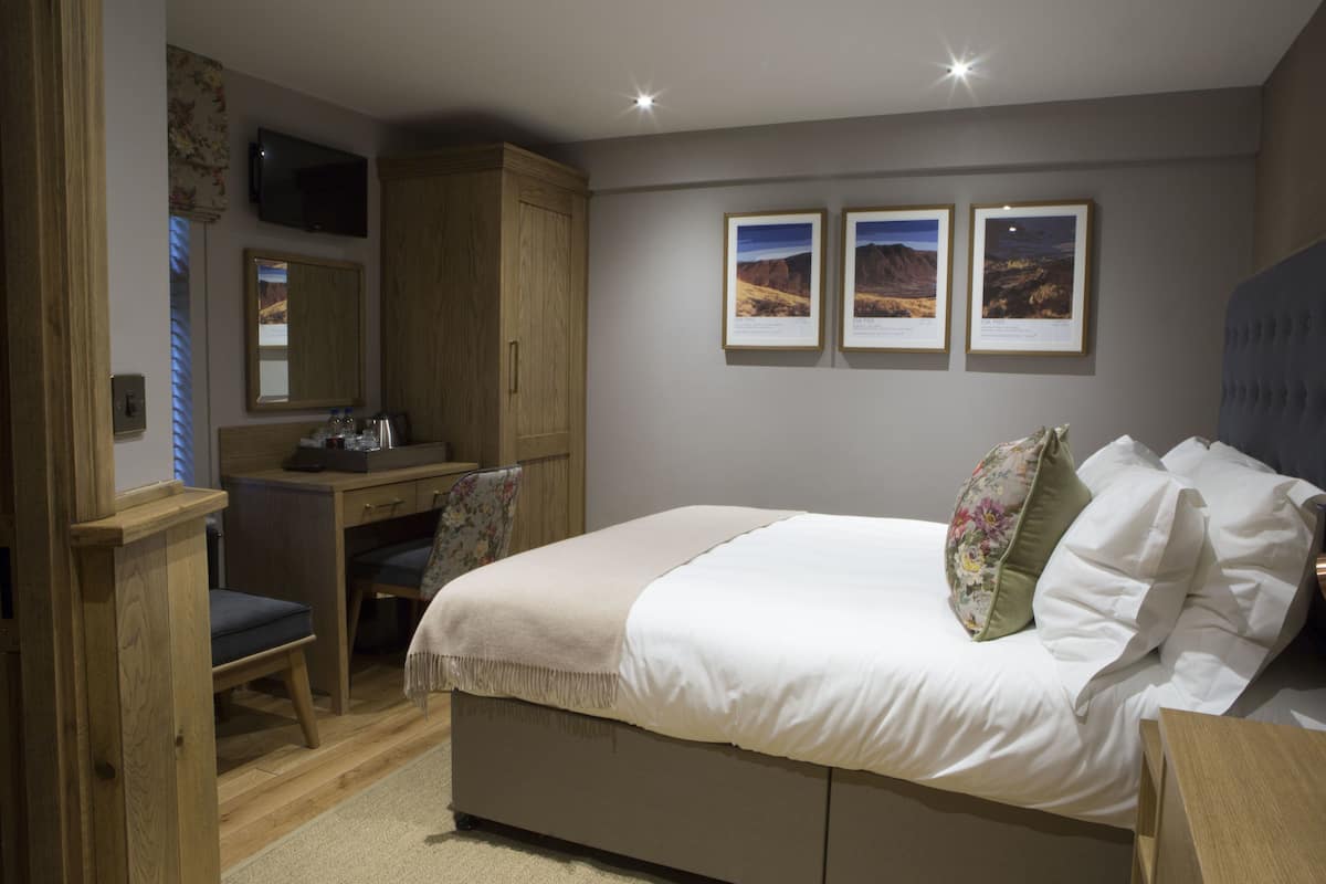 A bedroom with a bed, a desk, a chair, a television, and framed pictures on the wall.