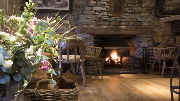 Una habitación acogedora con chimenea de piedra, sillas de madera, una cesta de mimbre y un letrero de precaución.