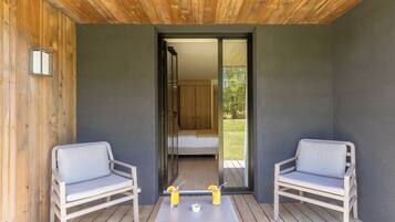 Een balkon met twee stoelen en een tafel, een schuifdeur naar een slaapkamer en een klein raam aan de linkerkant.