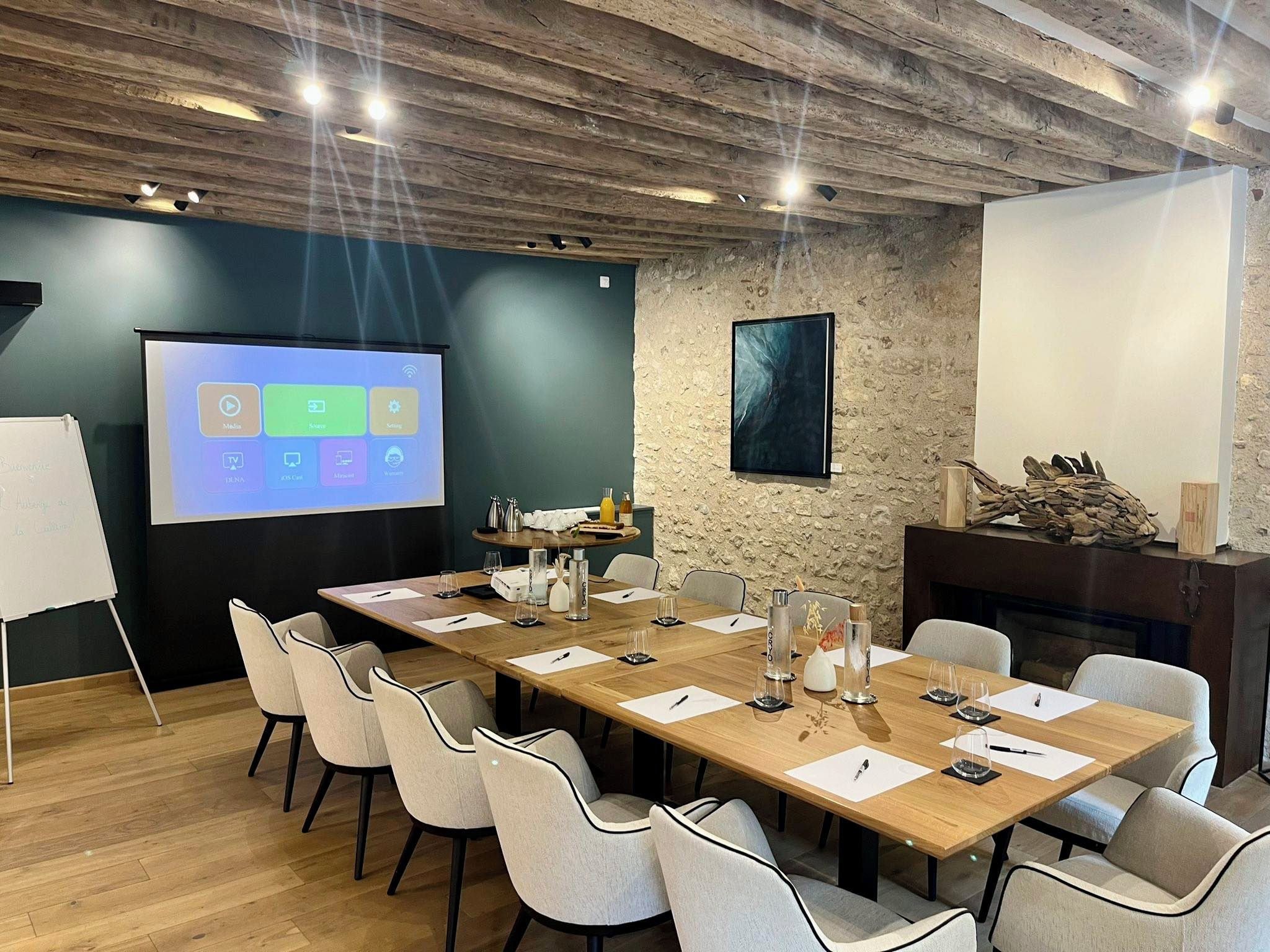 A conference room with a long table, chairs, a projector screen, and a stone wall.