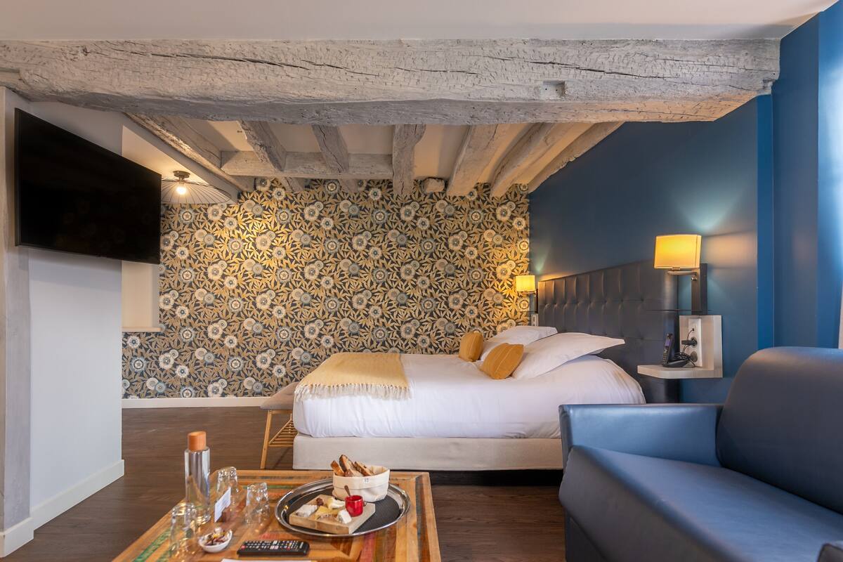 Ein Hotelzimmer mit einem Bett, einem Sofa, einem Couchtisch mit Frühstücksangeboten, einem Fernseher und einer Wand mit Muster.
