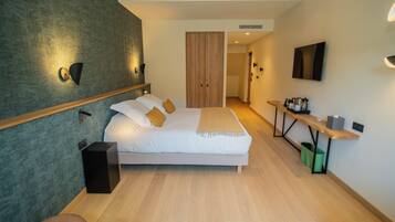 A modern hotel room with a large bed, a desk with a chair, a TV, and a wardrobe.