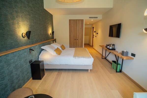 Una habitación de hotel moderna con una cama grande, un escritorio con silla, un televisor y un armario.