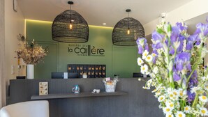 Un espace d’accueil agrémenté d’un mur végétal, d’un comptoir de réception, de deux lampes noires suspendues et d’un vase rempli de fleurs violettes.