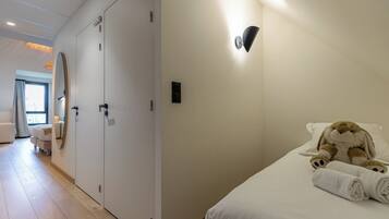 A hotel room with a bed, a teddy bear, a rolled towel, a wall-mounted light, and a large mirror.