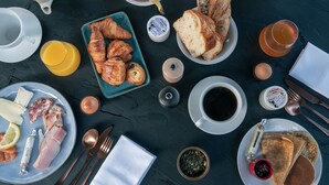 Une table de petit-déjeuner avec des croissants, du pain, des fruits et des boissons, le tout disposé sur une table sombre.