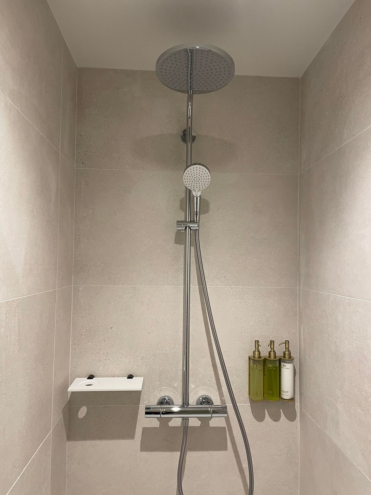Une douche équipée d’un pommeau de douche à main, d’un panneau de commande mural et d’une étagère pour les articles de toilette.